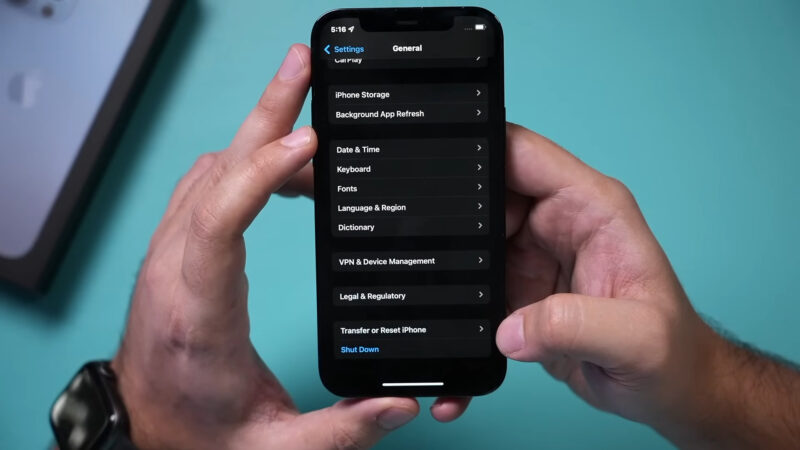 Hands holding an iPhone displaying the "General" settings menu with options like Date & Time, Keyboard, and Reset