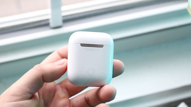 A Person Holding an AirPods Case, with The Lid Closed, Near a Window