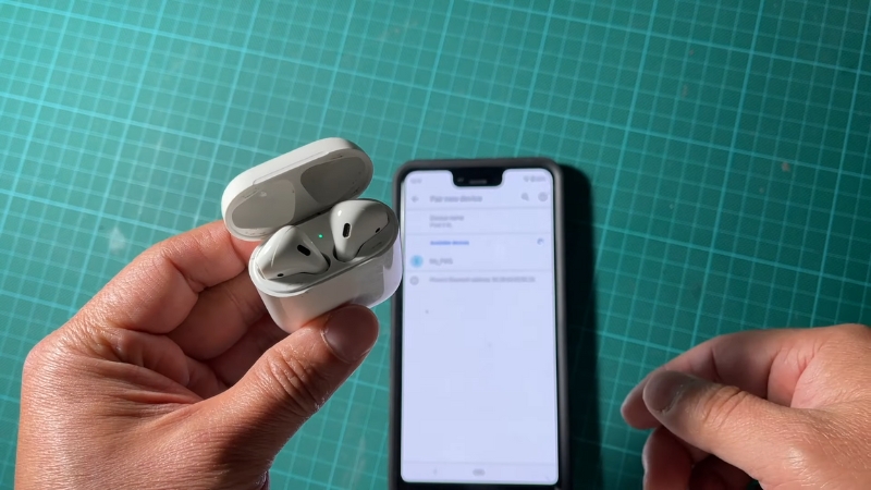 A Person Holding an Open AirPods Case Next to A Phone Showing Bluetooth Settings