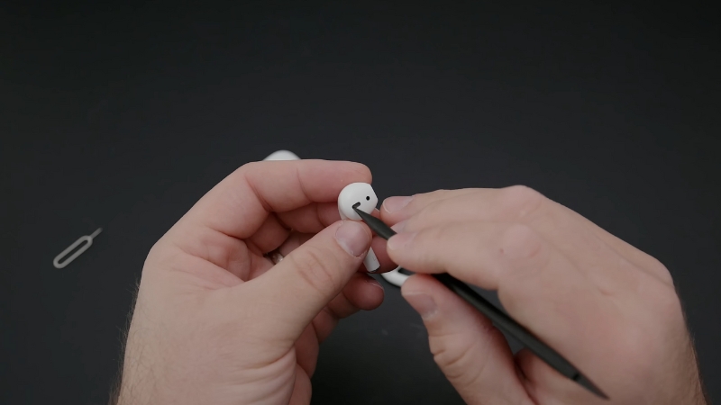 A Person Is Carefully Cleaning an AirPod Using a Small Tool to Remove Dirt or Debris