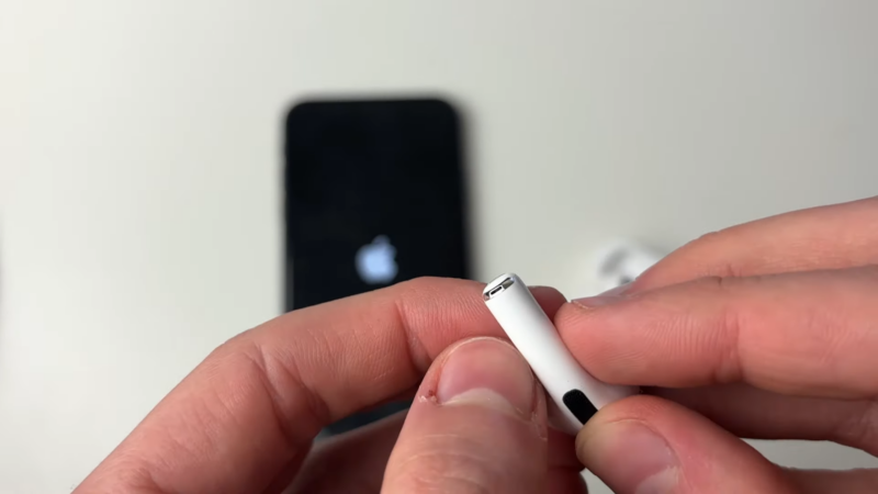 A Person Is Inspecting an AirPod, Holding It Near an iPhone